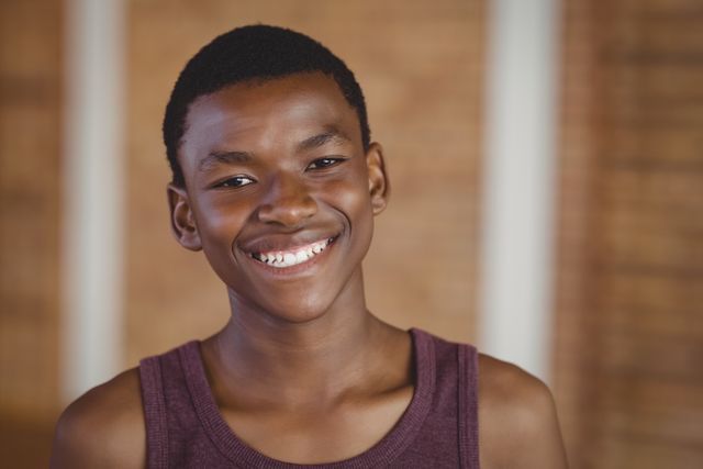 This image captures a smiling high school boy standing in a sports court. Ideal for use in educational materials, youth sports promotions, and articles about teenage life and confidence.