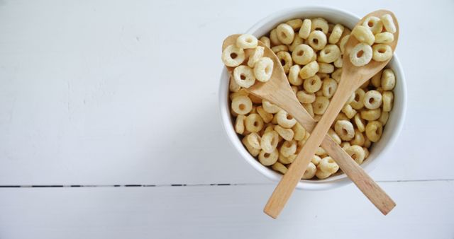 Perfect for healthy lifestyle and breakfast-themed promotions, this image features a bowl of cereal with two wooden spoons on a white table, adding a fresh and clean look ideal for food blogs, magazines, or advertisements showcasing breakfast food options.