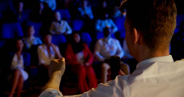 Business professional giving a presentation to an engaged audience in a darkened auditorium. Ideal for use in promotional materials, educational content, corporate training resources, conference brochures, and seminar announcements.