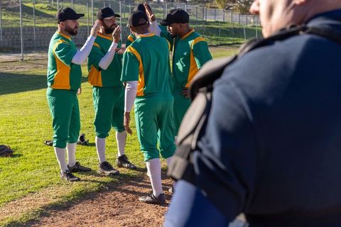 Multiracial baseball team huddling and high-fiving on infield showing teamwork