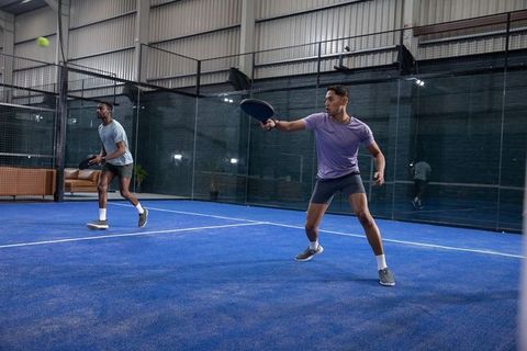 Diverse partners playing padel on indoor blue court, lunging to return fast volley