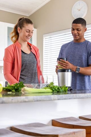 Couple preparing green smoothie in modern kitchen with african american man using blender