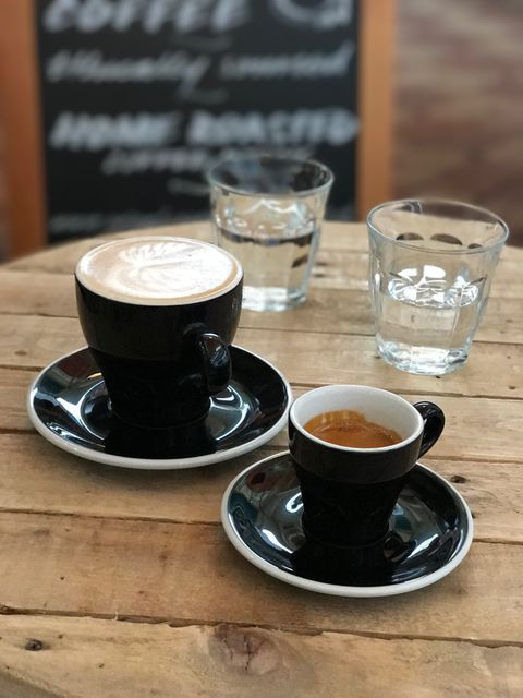 Coffee cups with latte art and espresso on rustic wooden table with glasses of water in café. Ideal for use in advertisements for cafés, coffee shops, or related to coffee culture. Perfect for blogs or articles discussing coffee, caffeine habits, and relaxing environments.