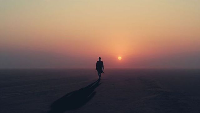 Walking solitary man crossing salt flat toward sunset with long shadow