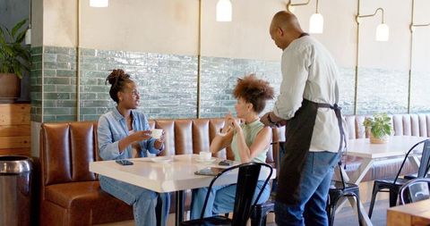 African american women chatting and sipping coffee with server at modern cafe booth