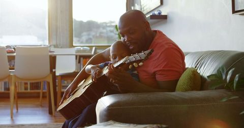 Father teaching son guitar at home cozy moment