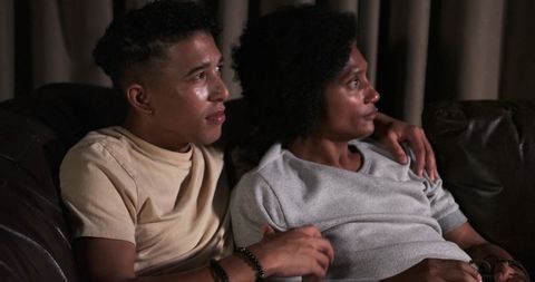 Intimate couple embracing on leather couch watching movie together in cozy warm low light