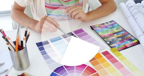 Kid comparing colorful paint fan decks and swatch palette at home design desk