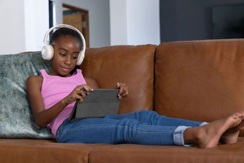 African american girl relaxing on couch using tablet with headphones