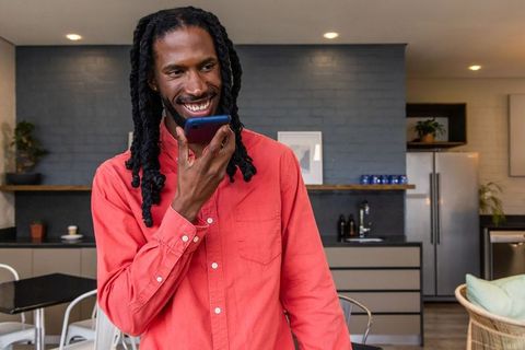 African American man speaking into smartphone and smiling in modern kitchen