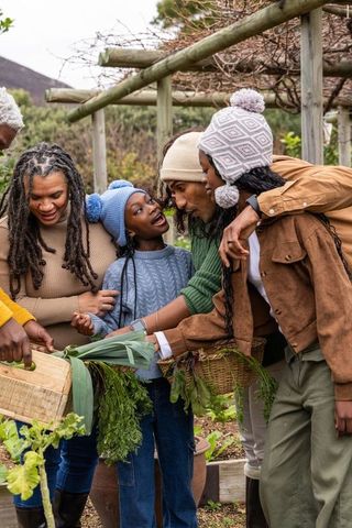 Multigenerational african american family harvesting vegetables in cozy backyard garden