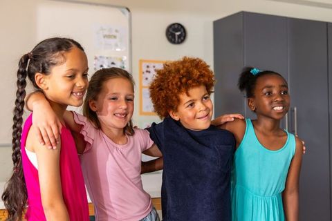 Diverse elementary kids smiling arm-in-arm in classroom showing friendship and teamwork