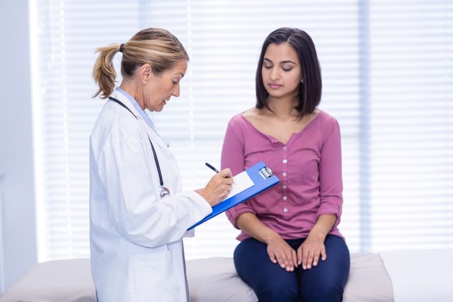 Doctor consulting with female patient in a clinical setting. Ideal for use in healthcare, medical, and wellness-related content. Can be used in articles, brochures, and websites focusing on patient care, medical consultations, and health services.