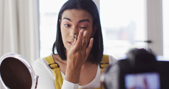 Youthful person applying eye makeup while recording a beauty tutorial for an online video. Ideal for promotions related to cosmetics, makeup tutorials, influencer marketing, self-care and fashion blogging.