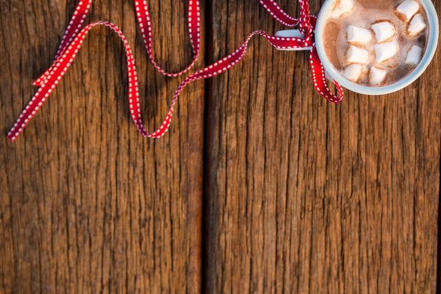 Cup of coffee with sugar cube tied with red ribbon on wooden plank during christmas time