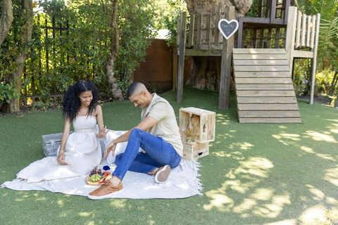 Expecting couple enjoying romantic backyard picnic by wooden treehouse, maternity celebration