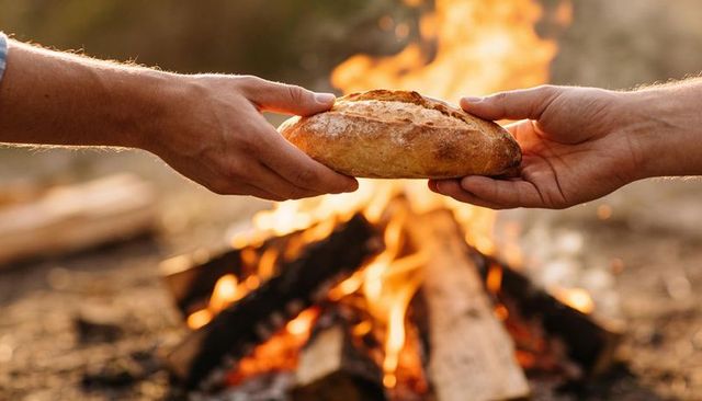 Hands exchanging crusty loaf over campfire creating warm rustic outdoor gathering