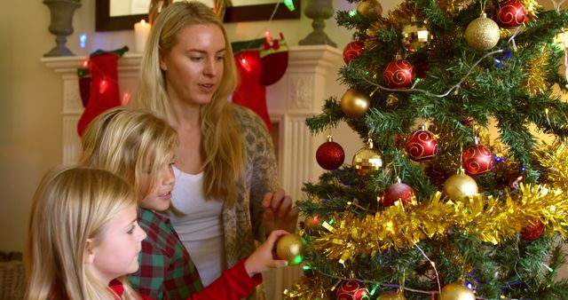 Caucasian woman with children decorates a Christmas tree at home. They share a festive moment, adding ornaments and tinsel together.