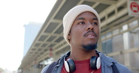 Young african american commuter waiting on transit platform wearing beanie and headphones