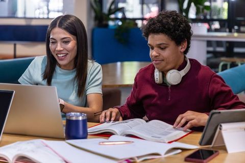 Smiling diverse students collaborating on laptops and textbooks in campus study lounge