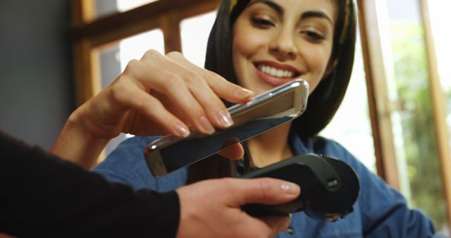 Young Hispanic or Latino woman processes a mobile payment at a store. She exemplifies modern payment technology in a retail setting.