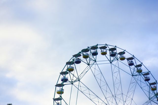 Colorful Ferris wheel against cloudy sky suggesting a fun and leisurely time at an amusement park or carnival. Suitable for use in themes related to entertainment, recreation, family outings, and travel brochures promoting fairgrounds or amusement parks.