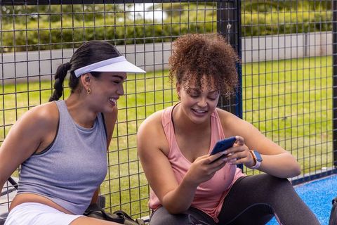 African american women relaxing on court sideline checking phone after workout
