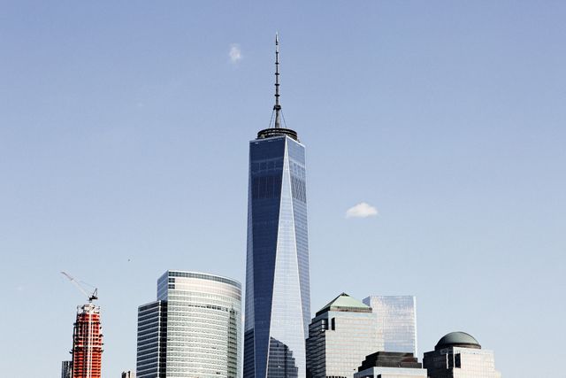 This image portrays a prominent modern skyscraper towering against a clear blue sky in an urban cityscape. This photo is ideal for use in real estate, architecture, construction, finance, and urban planning projects. It could be used in marketing materials, presentations, websites, and articles that highlight modern architecture, business districts, and metropolitan development.