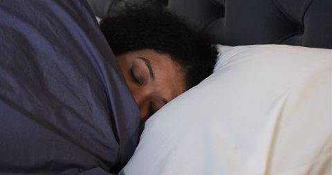 Mid-adult african american woman resting under dark gray duvet on white pillow, serene