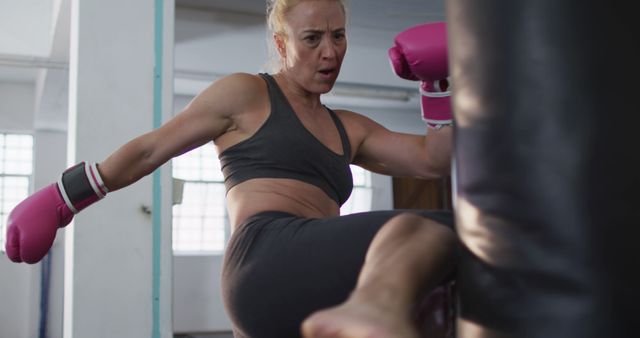 Caucasian female boxer wearing boxing gloves kicking the punching bag at the gym. sports, training and fitness concept