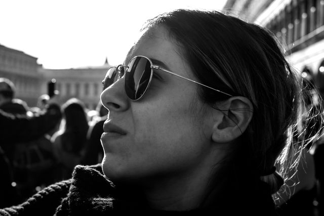 Close-up portrait of a woman wearing sunglasses, outdoors, in a busy urban environment. Ideal for use in fashion, streetwear, city life blogs, personal expression, and editorial content showcasing style and urban culture.