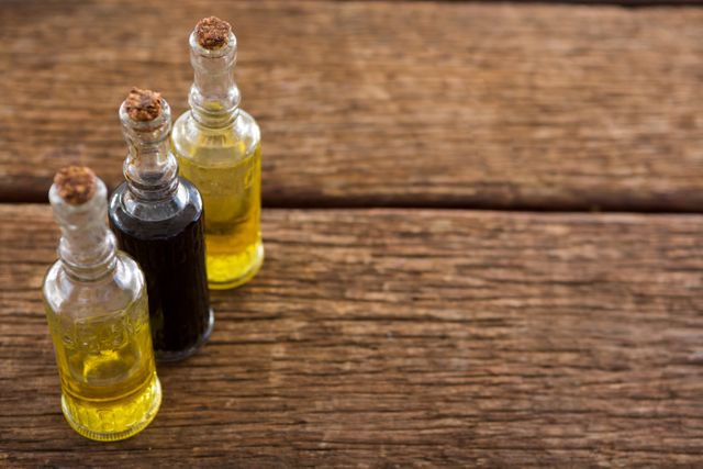 Close-up of olive oil and balsamic vinegar in glass bottles with cork stoppers on a rustic wooden table. Ideal for use in culinary blogs, cooking websites, healthy eating promotions, and organic food advertisements.