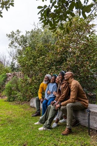 Multigenerational african american family sitting on log bench smiling in lush garden