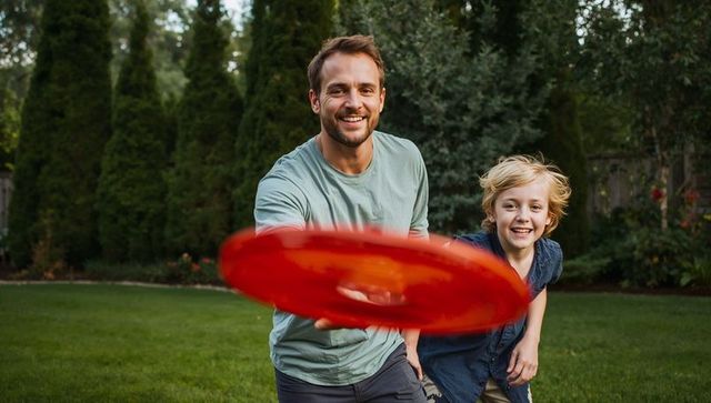 Father and son playing frisbee in backyard, smiling and chasing red disc, outdoor family activity