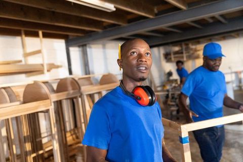 African american woodworkers building chair frames in rustic workshop with ear protection