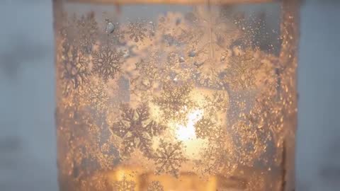 Revealing snowflake-frosted jar at window with warm candle glow and water droplets