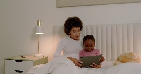 Mother and daughter spending time with tablet in cozy bedroom
