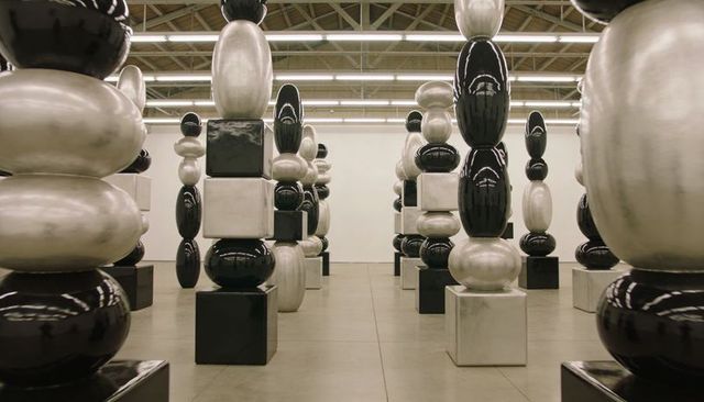 Monochrome stacked sculptural columns in symmetrical gallery with reflective surfaces
