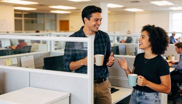 Smiling coworkers chatting over coffee in modern open-plan office