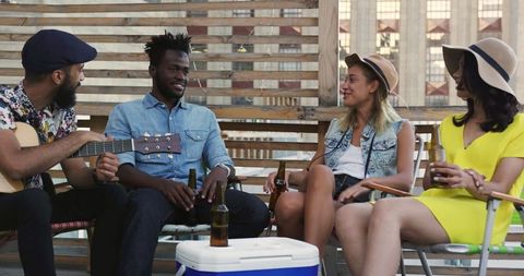 Diverse friends enjoying rooftop party with guitar and drinks