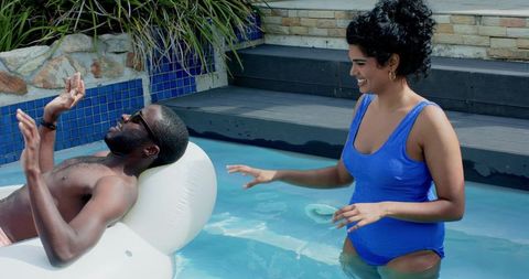 Diverse couple relaxing in backyard pool with white inflatable lounger and swimwear