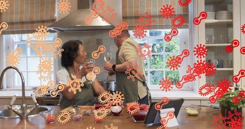Mature couple cooking together at kitchen island, enjoying wine and meal prep with tablet