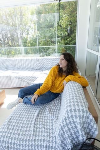Young woman relaxing on sofa in sunroom wearing mustard sweater and houndstooth throw