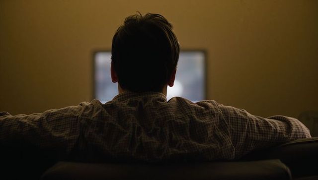 Backlit man watching tv on sofa at night with blue screen glow and moody quiet atmosphere