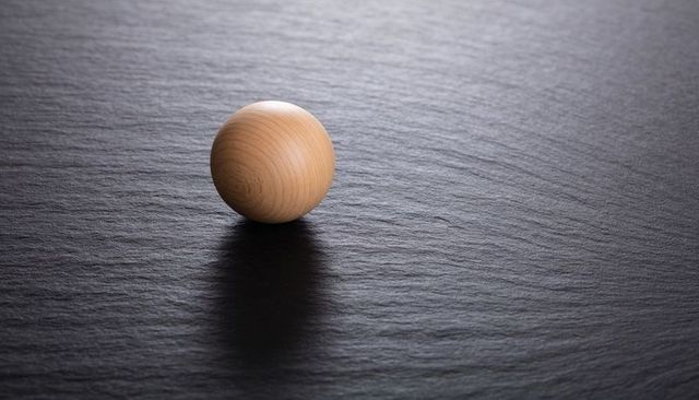 Minimalist polished wooden sphere on dark slate surface with soft shadow and texture