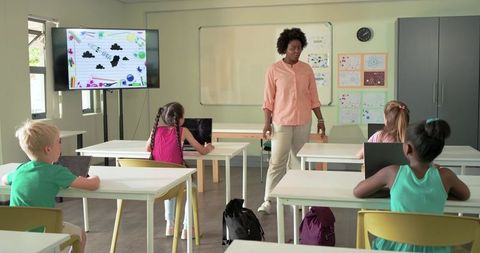 African American teacher leading elementary classroom while students working on tablets