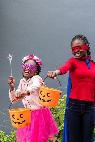 African american girls celebrating halloween in colorful tutus and capes holding jack-o-lantern buck