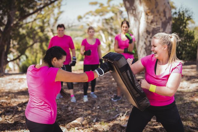 Women engaged in boxing training during an outdoor boot camp on a sunny day. Ideal for illustrating group fitness activities, promoting health and wellness programs, showcasing teamwork and determination in a natural setting.