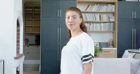 African american woman standing in modern living room wearing striped tee near bookshelves
