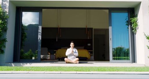 Woman Meditating on Home Doorway with Open Glass Doors